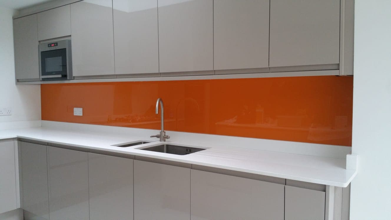 Orange coloured glass splashback above a white worktop between wall and base units